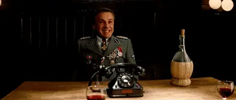 GIF: Mann in Uniform lacht an einem Tisch mit altem Telefon